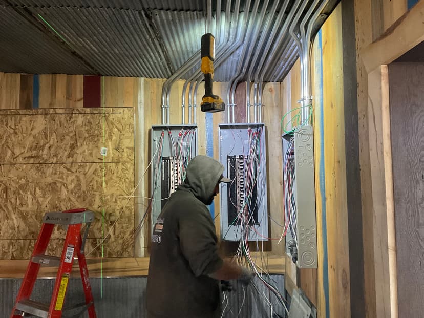 Electrician working on electrical panels in a construction site with wires and tools.
