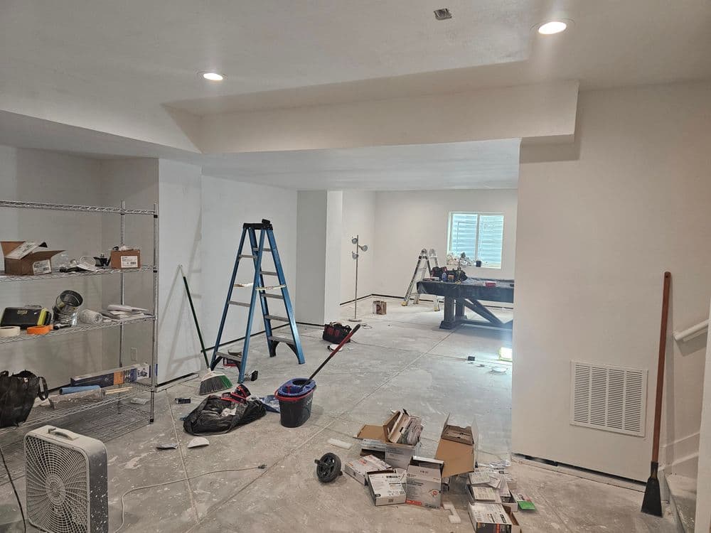 Renovated basement space with tools, ladders, and unfinished flooring. Bright white walls.